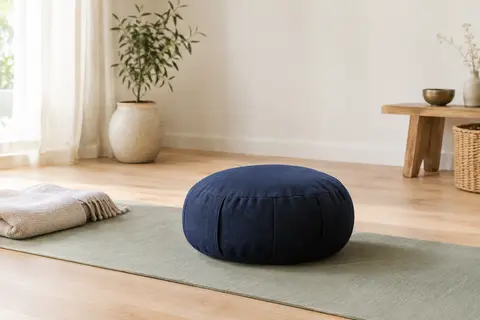 Coussin zafu bleu nuit en coton posé sur un tapis dans un studio lumineux au sol en bois clair.