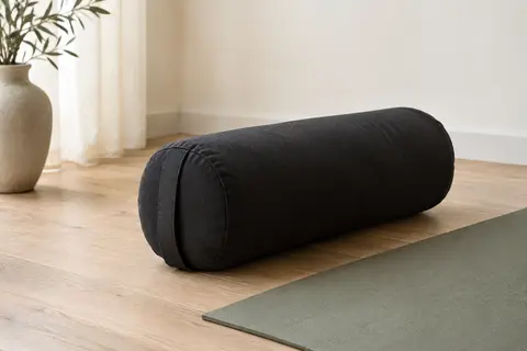 Bolster de yoga cylindrique noir en coton, posé près d’un tapis dans un studio lumineux.