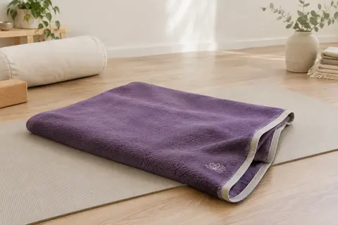 Couverture de yoga violette en polaire, avec bord contrasté et broderie lotus, posée sur un tapis.