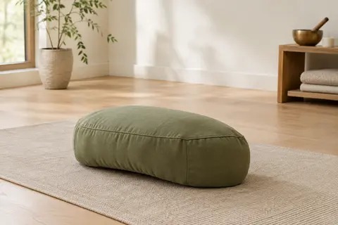 Coussin de méditation demi-lune vert olive en coton posé sur un tapis dans un studio lumineux
