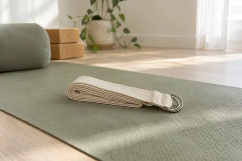 Sangle de yoga écrue en coton pliée sur un tapis, avec ses deux anneaux métalliques visibles.