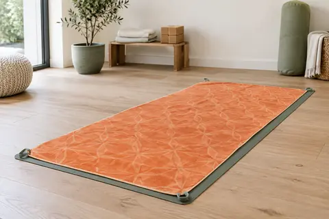 Serviette de yoga orange en microfibre étendue sur un tapis, avec ses coins de fixation visibles.