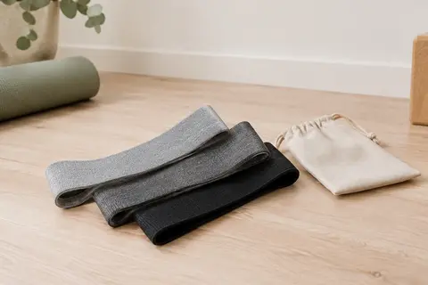 Trois bandes élastiques en tissu grises et noires avec leur sac, posées dans un studio lumineux.