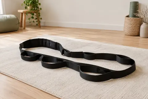 Sangle d’étirement noire à boucles posée sur un tapis écru dans un studio lumineux.