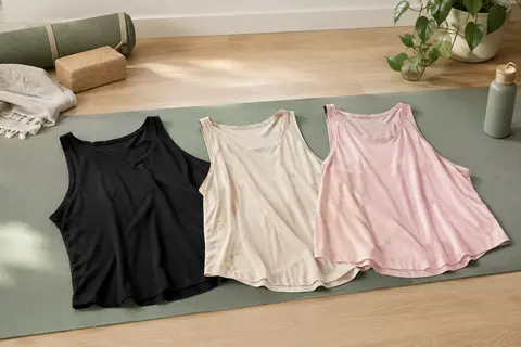 Trois débardeurs amples noir, beige et rose pâle disposés sur un tapis dans un studio lumineux.