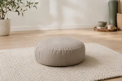 Coussin de méditation rond en coton taupe clair posé sur un tapis écru dans un studio lumineux.