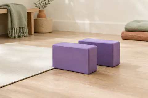 Deux briques de yoga violettes en mousse EVA posées près d’un tapis dans un studio lumineux au sol en bois clair.