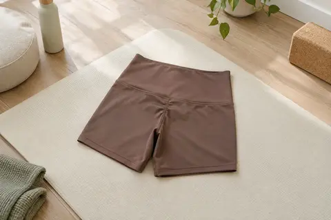 Short de sport brun moka à taille haute et détail froncé, posé sur un tapis écru en studio