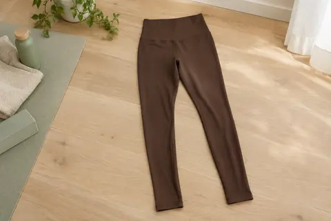 Legging de yoga marron café à taille haute, présenté à plat dans un studio lumineux au sol en bois clair.